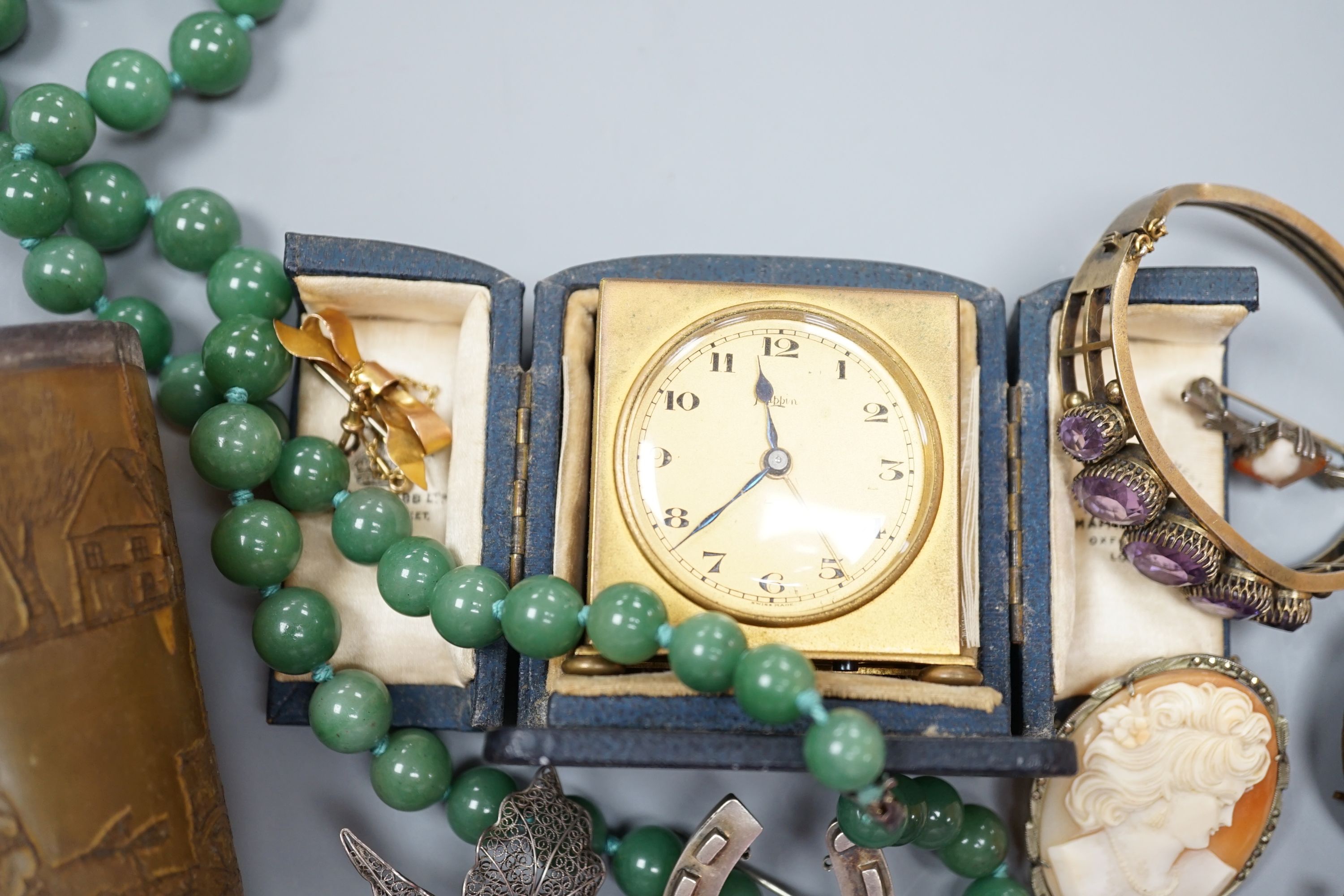 A small collection of jewellery including a silver horseshoe brooch, 9ct suspension brooch, gross 2.8 grams, and a travelling bedside timepiece and beaker.